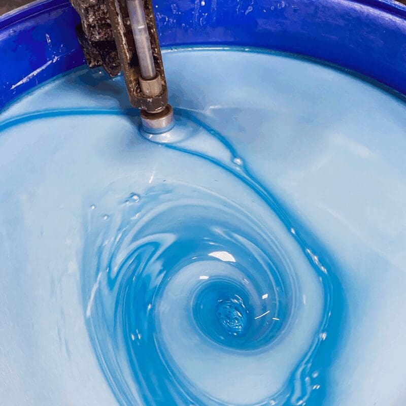 Water swirling in a blue container from a filling spout, creating concentric ripples and waves
