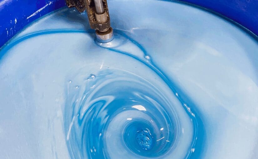 Water swirling in a blue container from a filling spout, creating concentric ripples and waves