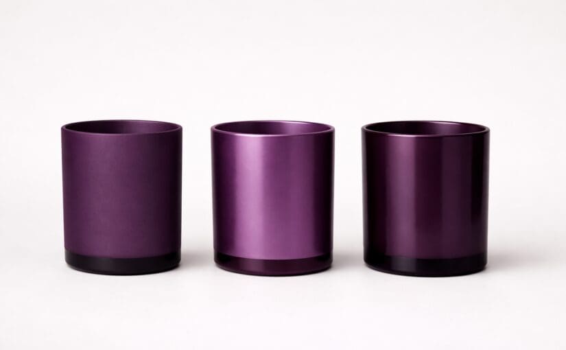 Three purple metallic cylindrical candle jars with black bases arranged in a row against a white background