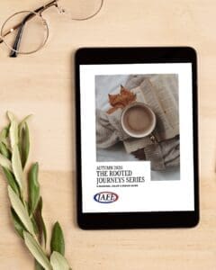 Tablet displaying autumn 2026 color guide for "The Rooted Journeys Series" with cozy styled photo of coffee cup and fall leaves, surrounded by glasses and plant leaves on wooden desk
