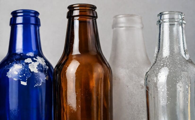 Four glass bottles in blue, brown, frosted, and clear with varying surface finishes and condensation, showcasing glass decorating and customization options
