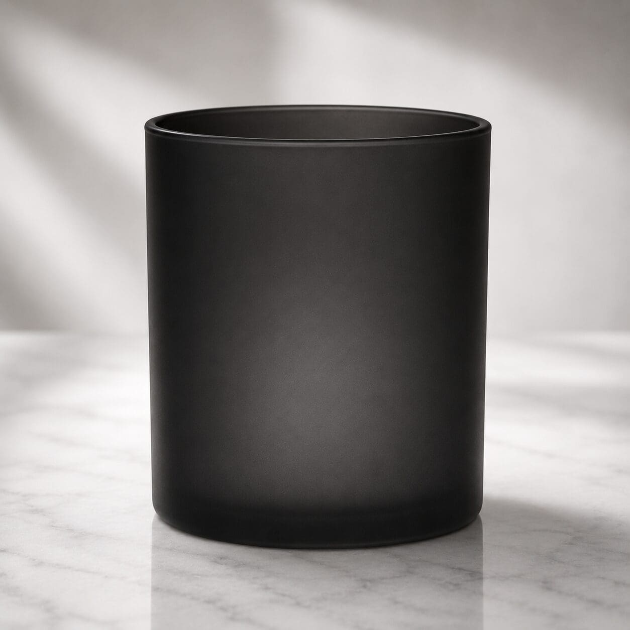 Black frosted glass cylinder on marble surface with soft natural lighting, ideal for candle jar decorating and glass screen printing applications