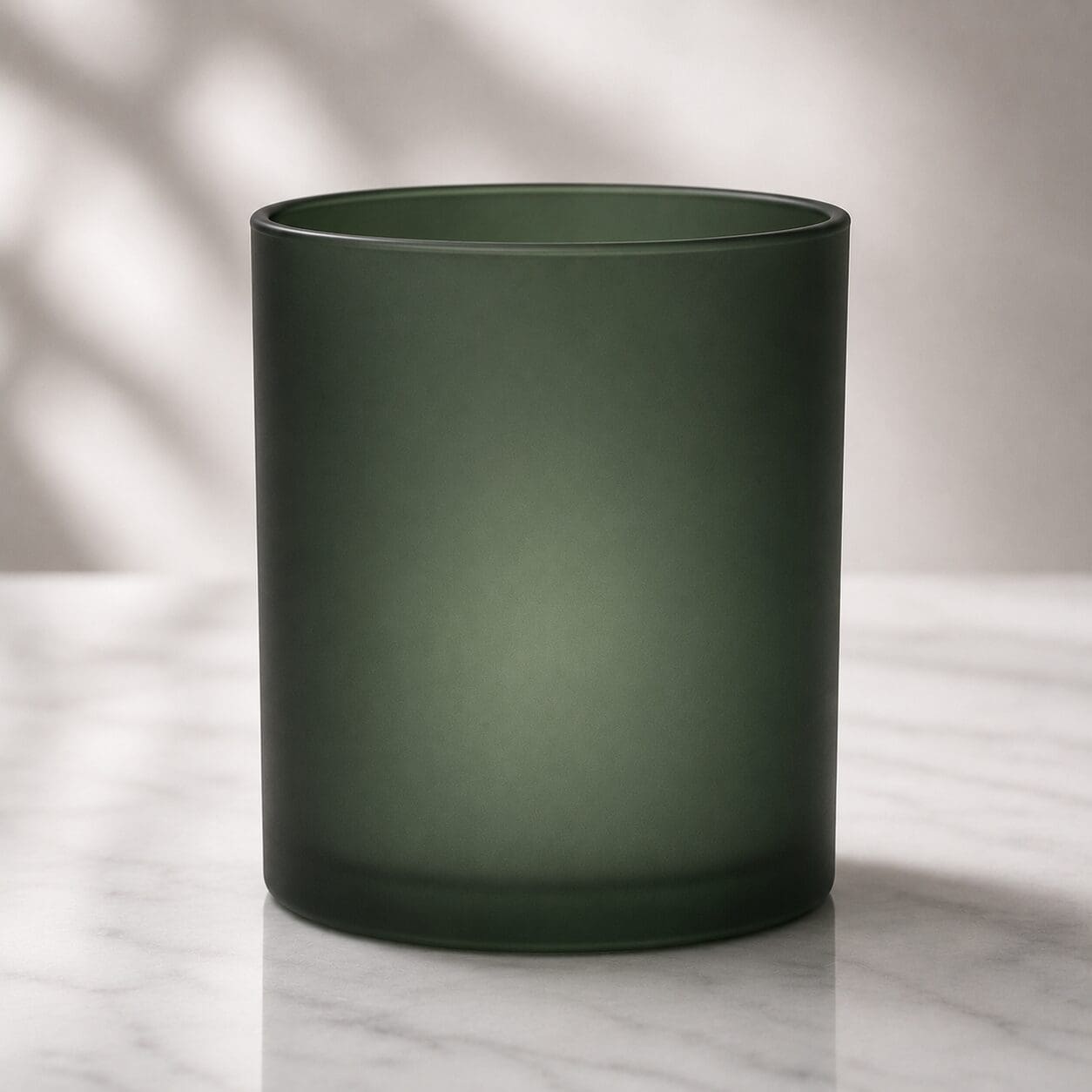 Frosted dark green glass cylinder container with smooth finish on marble surface, ideal for candle jar decorating or perfume bottle customization