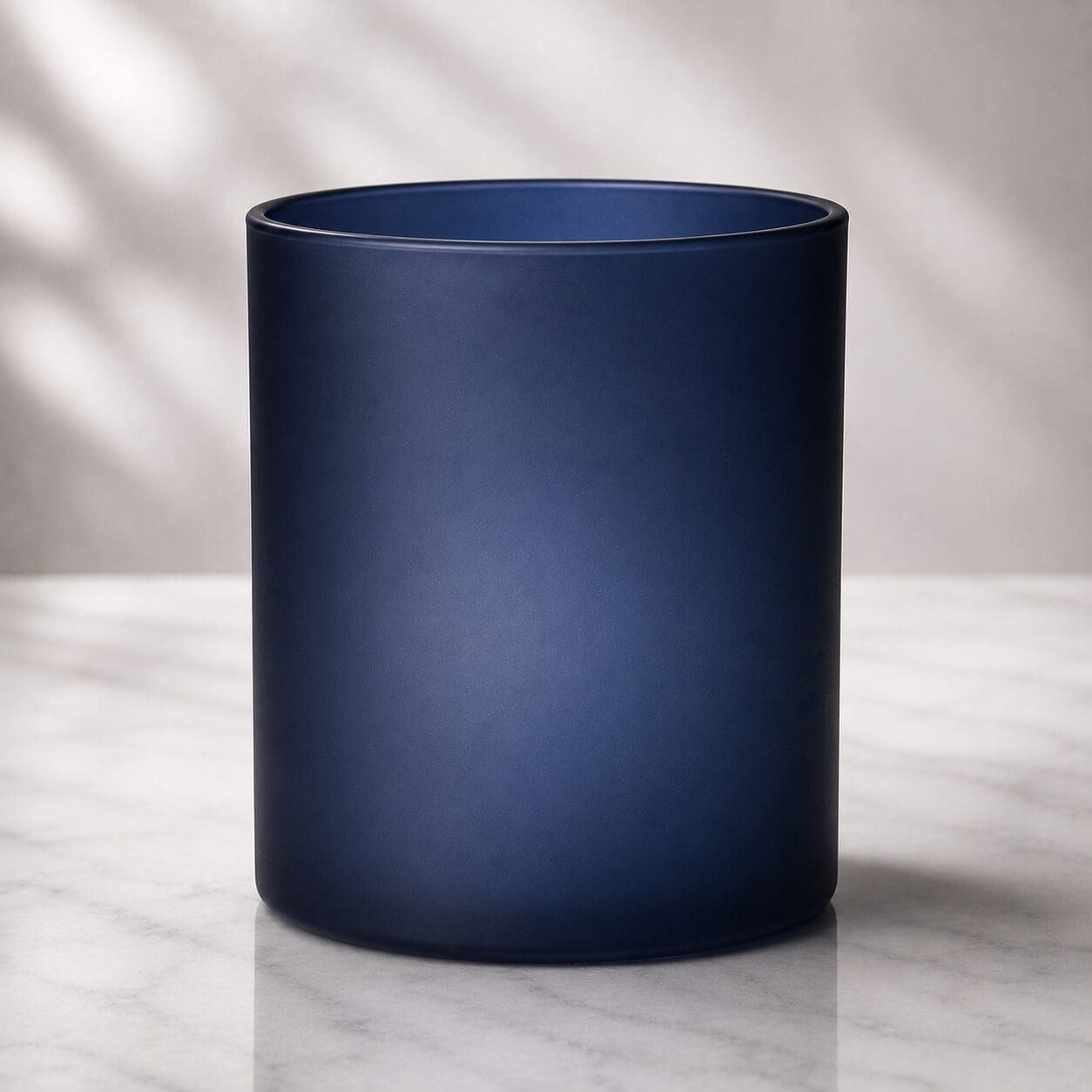 Dark blue frosted glass cylinder on marble surface with natural lighting and neutral background