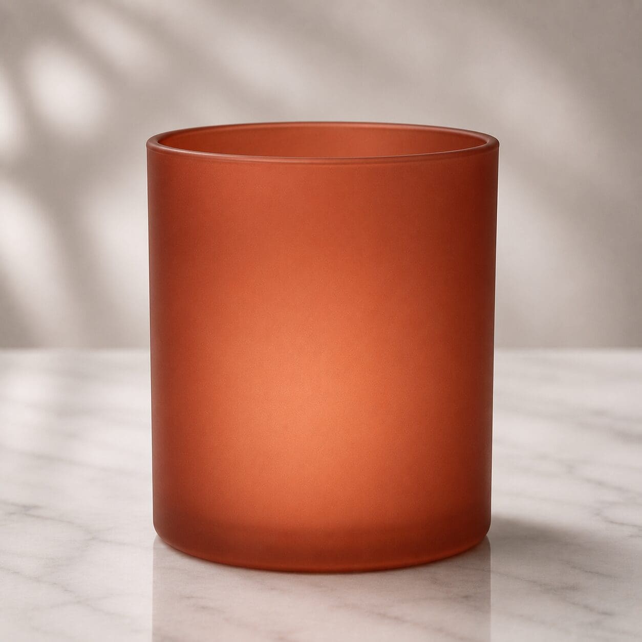 Red frosted glass cylinder vase on marble surface with soft natural lighting