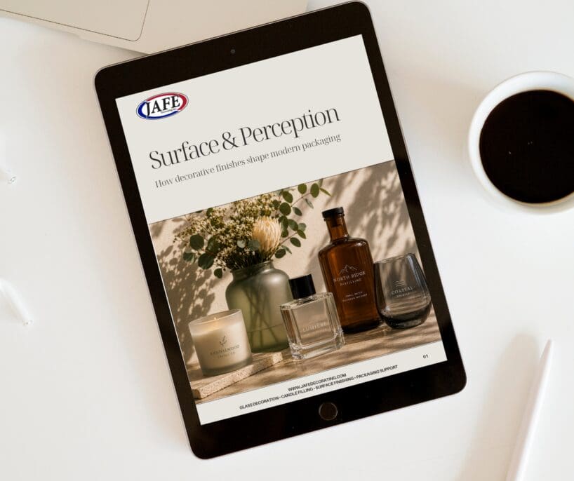 iPad displaying JAFE Surface & Perception guide on glass decorating and modern packaging, surrounded by coffee and decorated candles and bottles on desk