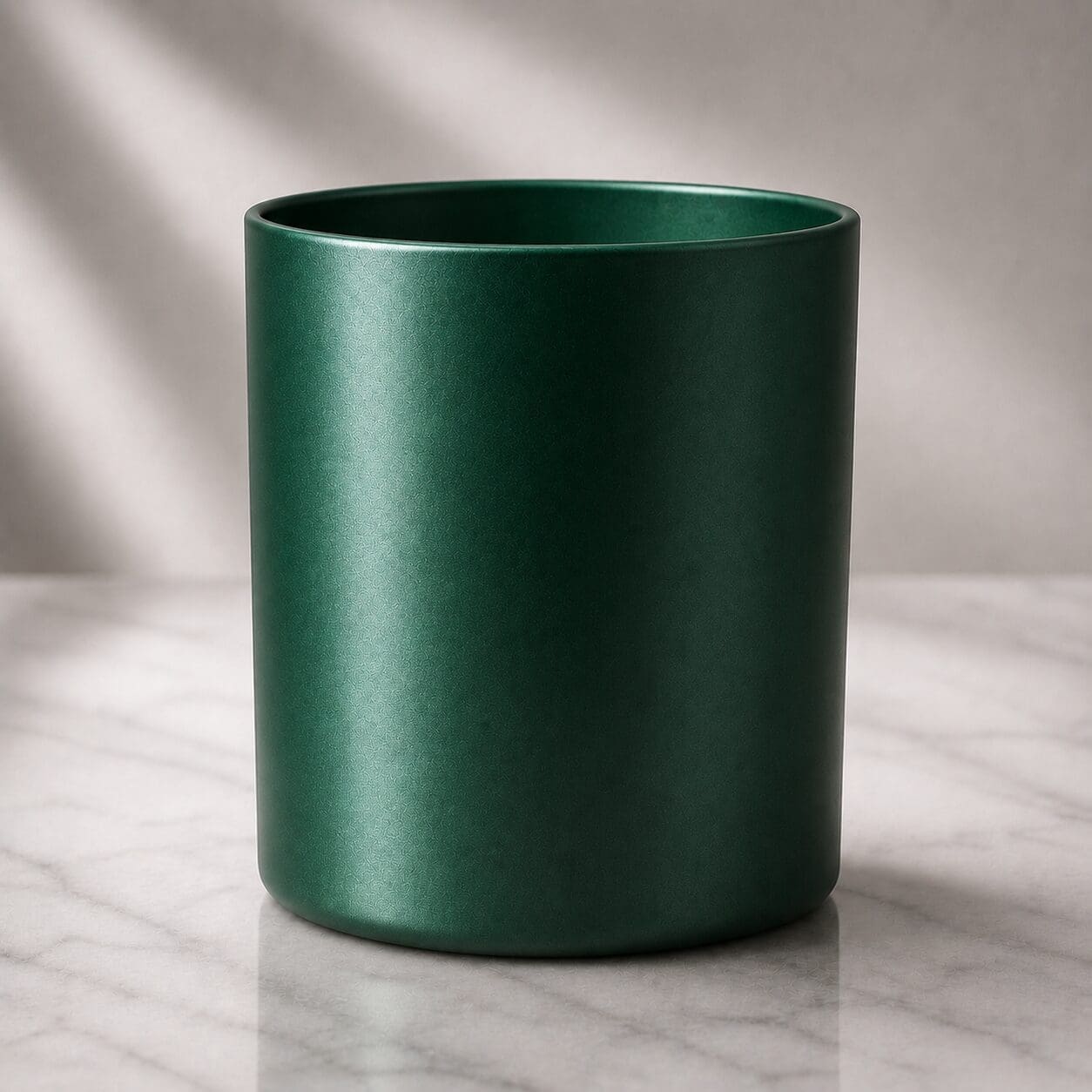 A deep green cylindrical ceramic or glass container with a matte finish, sitting on a marble surface under soft natural light