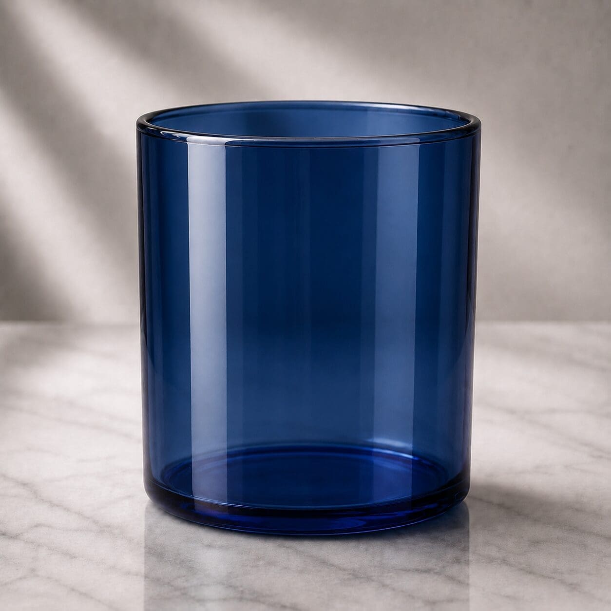 Empty cobalt blue glass cylinder jar on marble surface with natural lighting