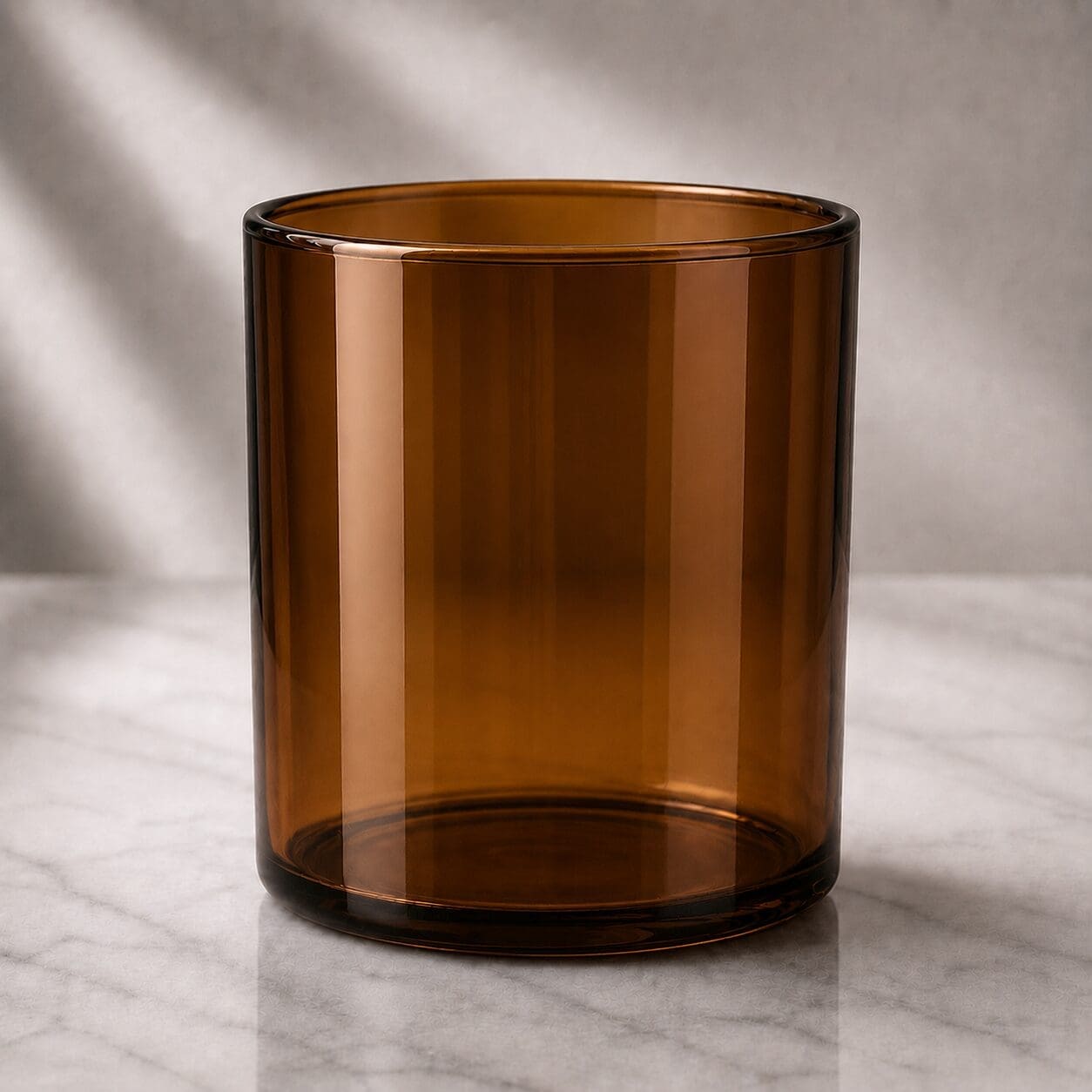 Empty amber glass cylinder on marble surface with soft natural lighting, suitable for candle jar decorating or perfume bottle customization