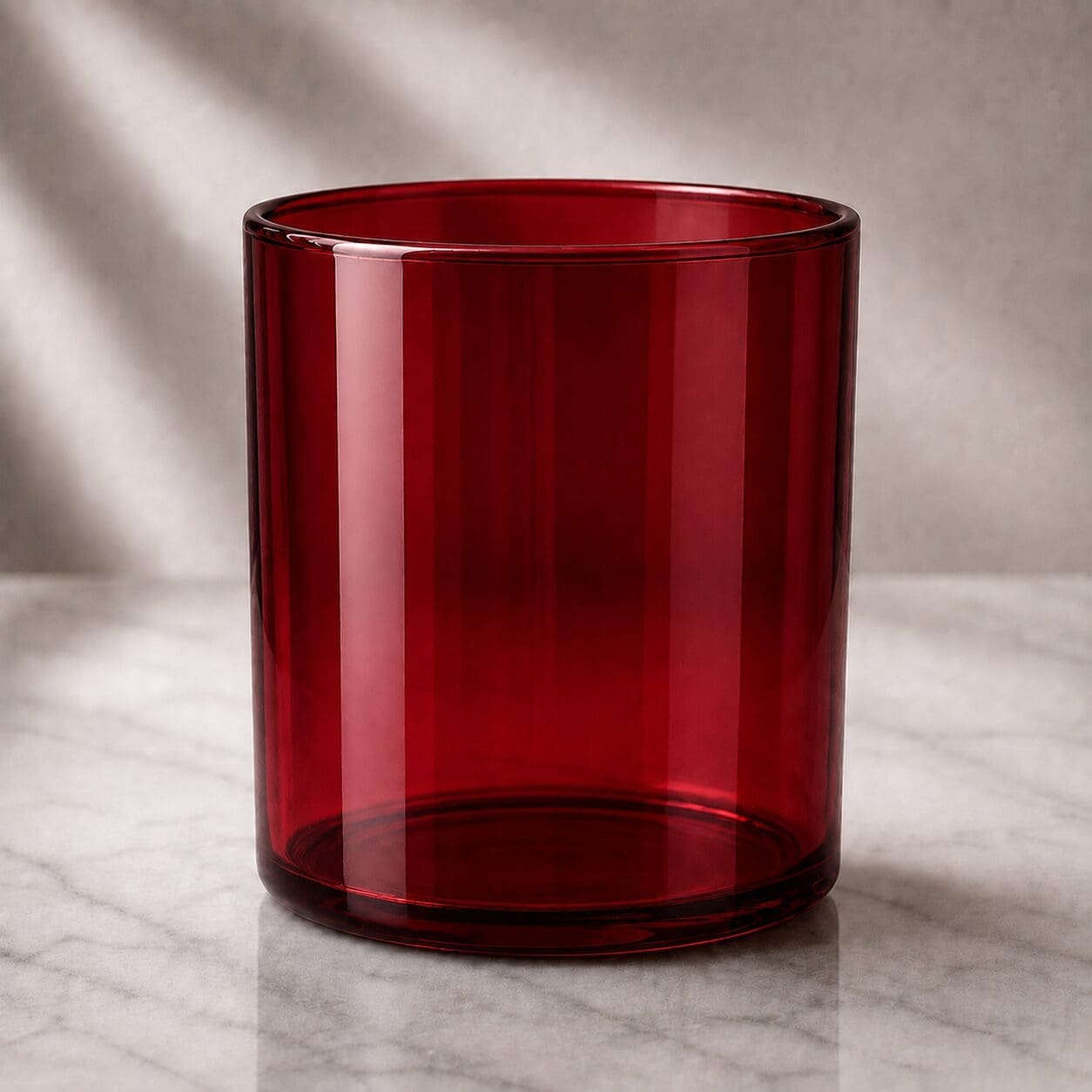 A deep red cylindrical glass jar with smooth walls positioned on a marble surface, ideal for candle filling services or decorative glass projects
