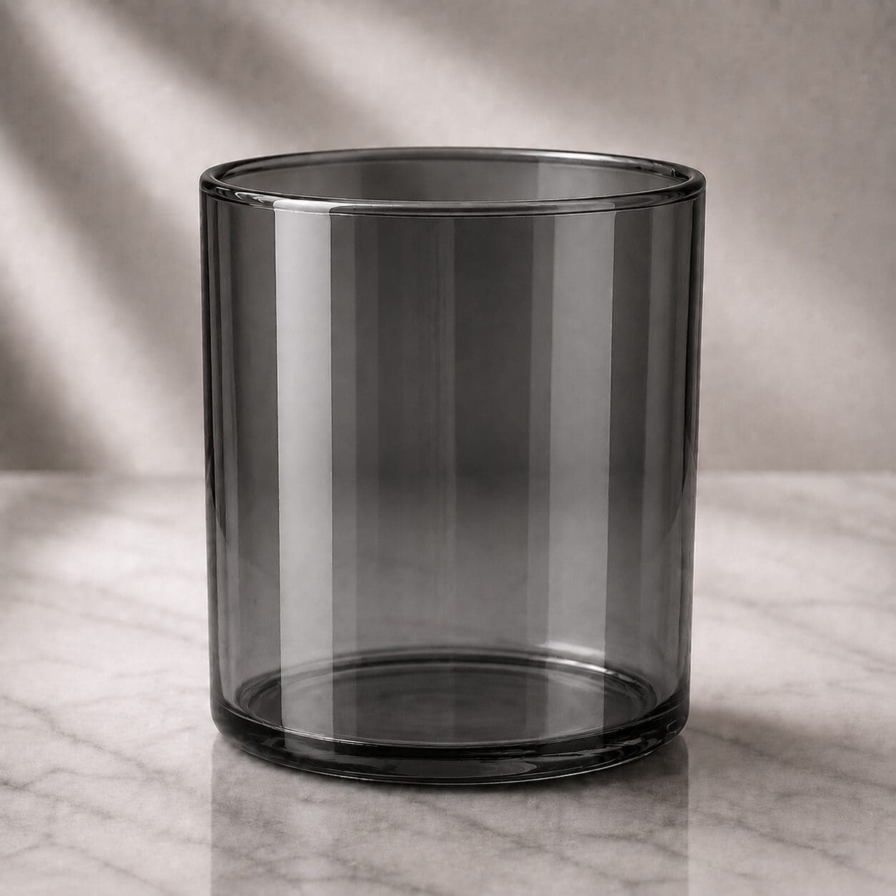 Empty black glass cylinder jar on marble surface with soft natural lighting