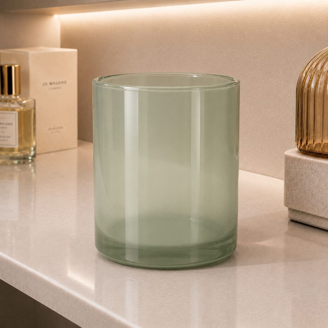 Frosted green glass candle jar displayed on white shelf with perfume bottle and gold decorative vase