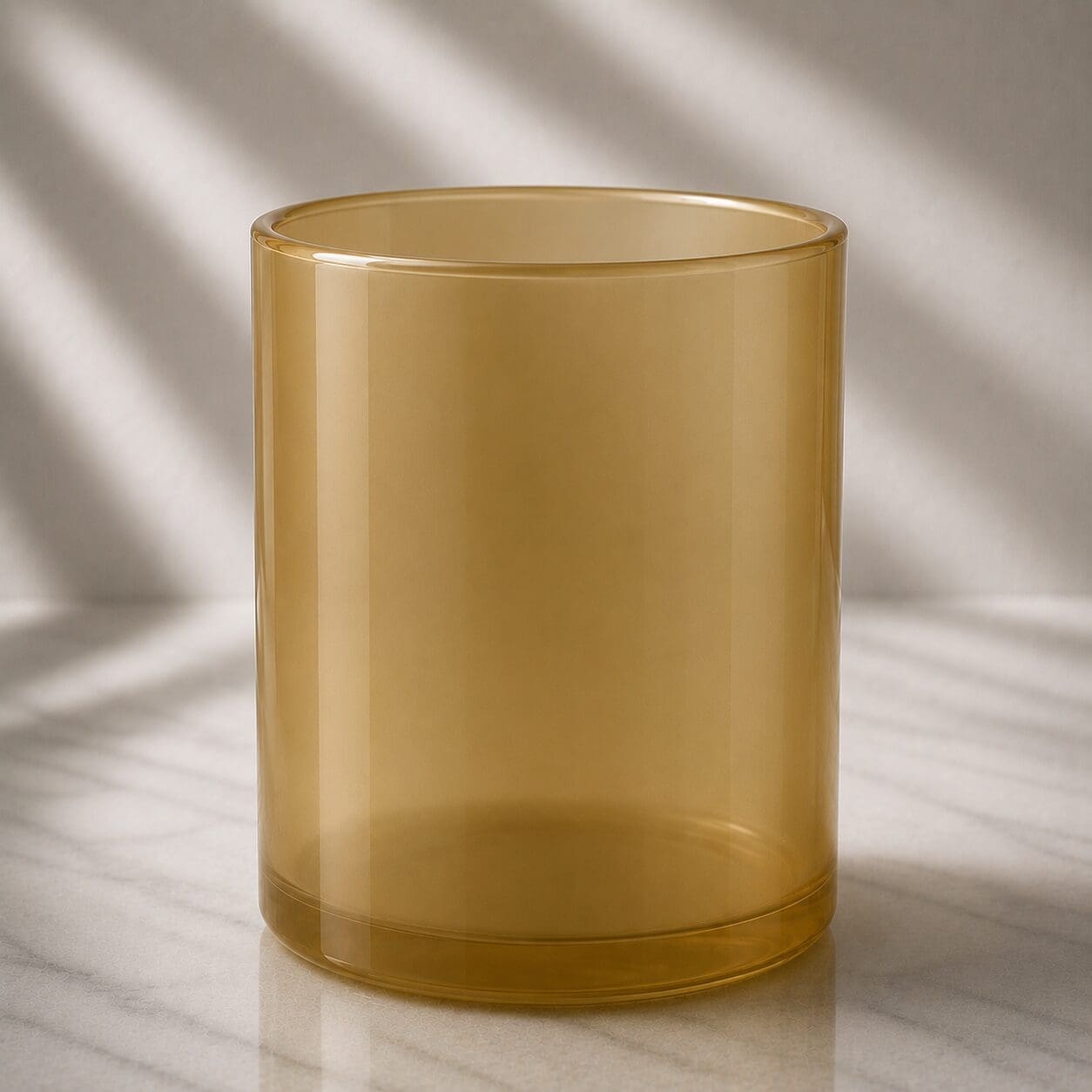 Empty amber glass cylinder jar on marble surface with natural light shadows in background