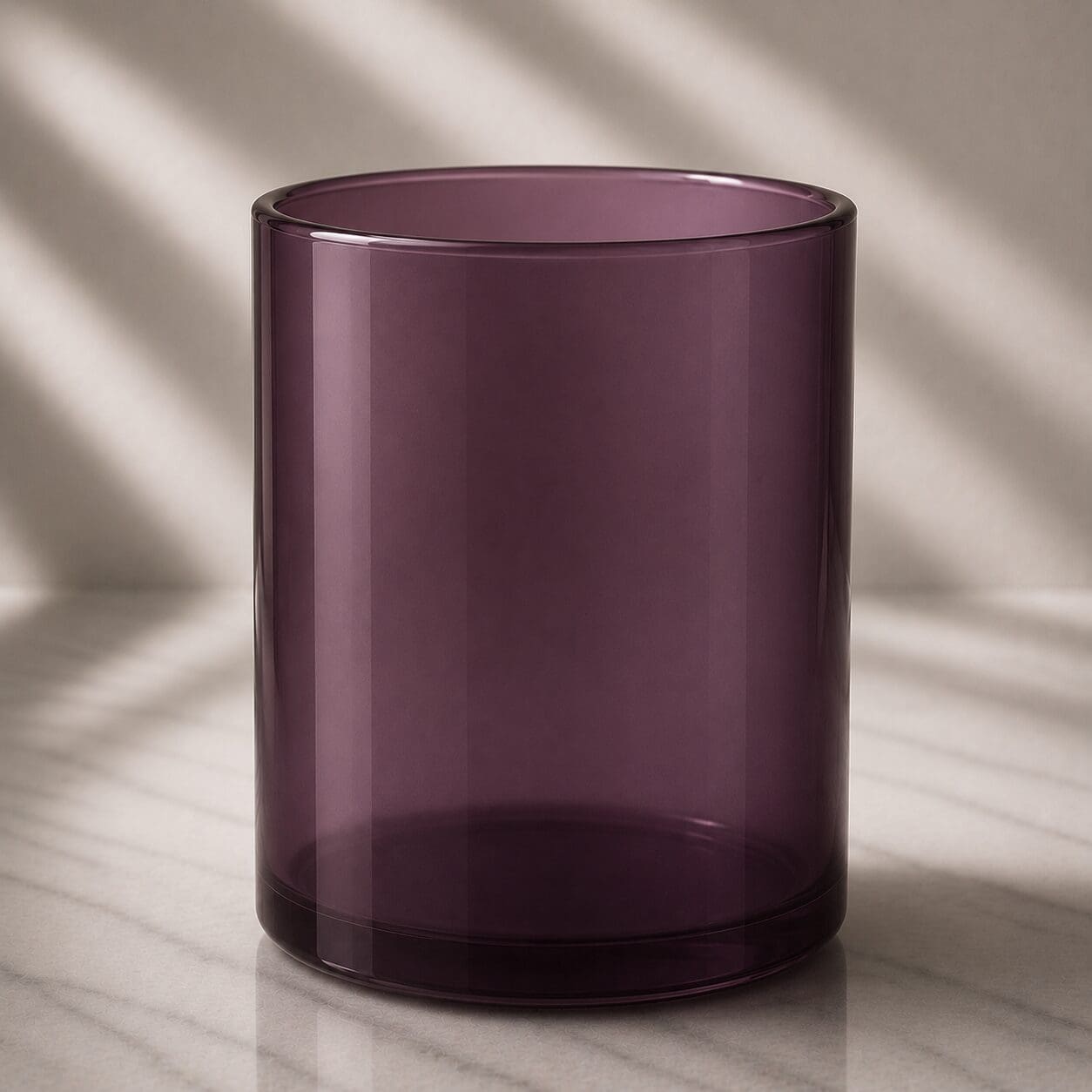 Empty burgundy glass cylinder on marble surface with soft natural lighting