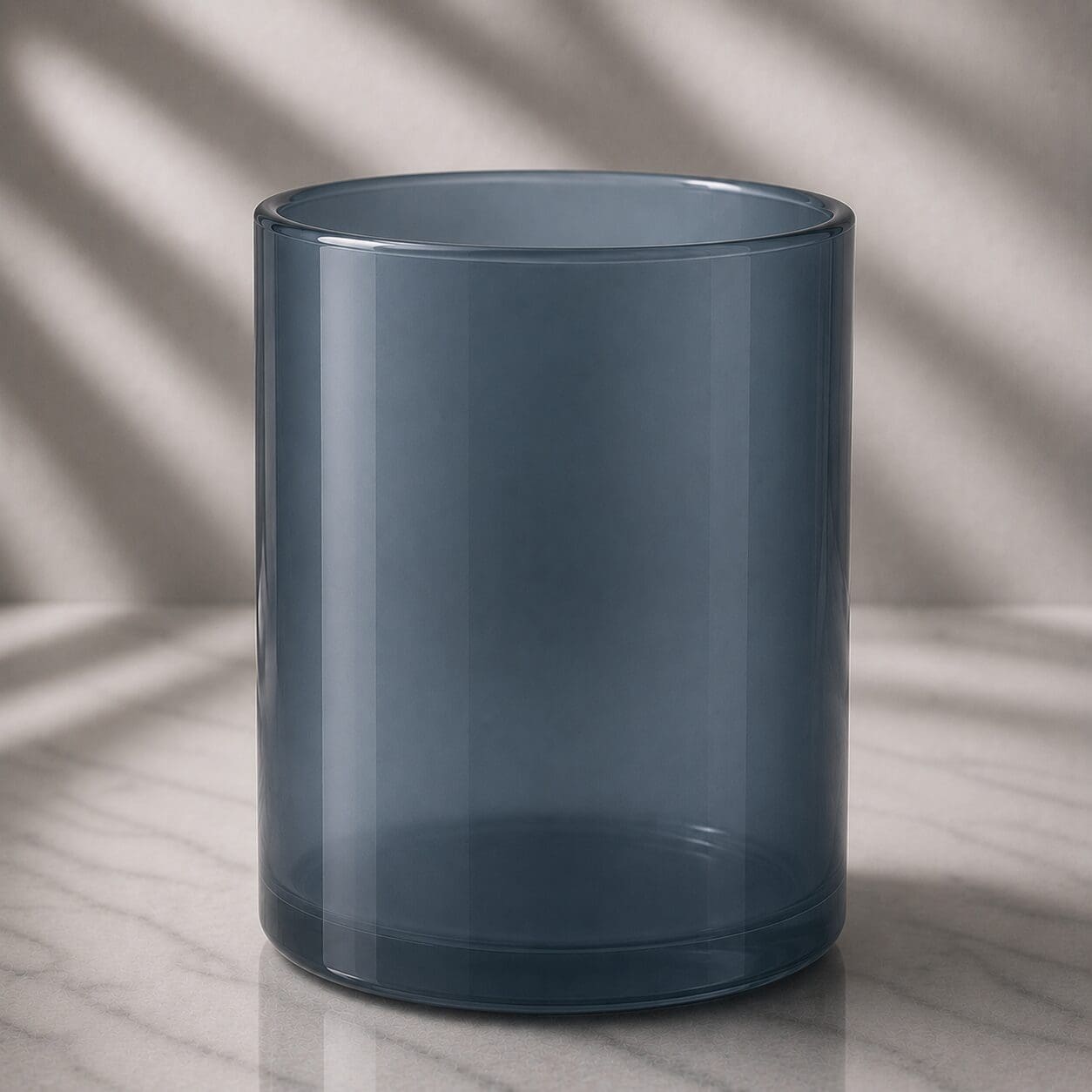 Empty frosted teal glass cylinder on marble surface with diagonal window shadows in background