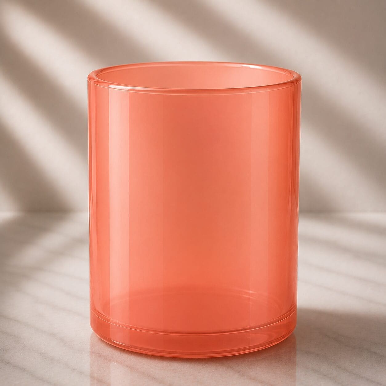 Translucent coral glass cylinder with smooth finish and rounded edges, displayed on marble surface with natural lighting