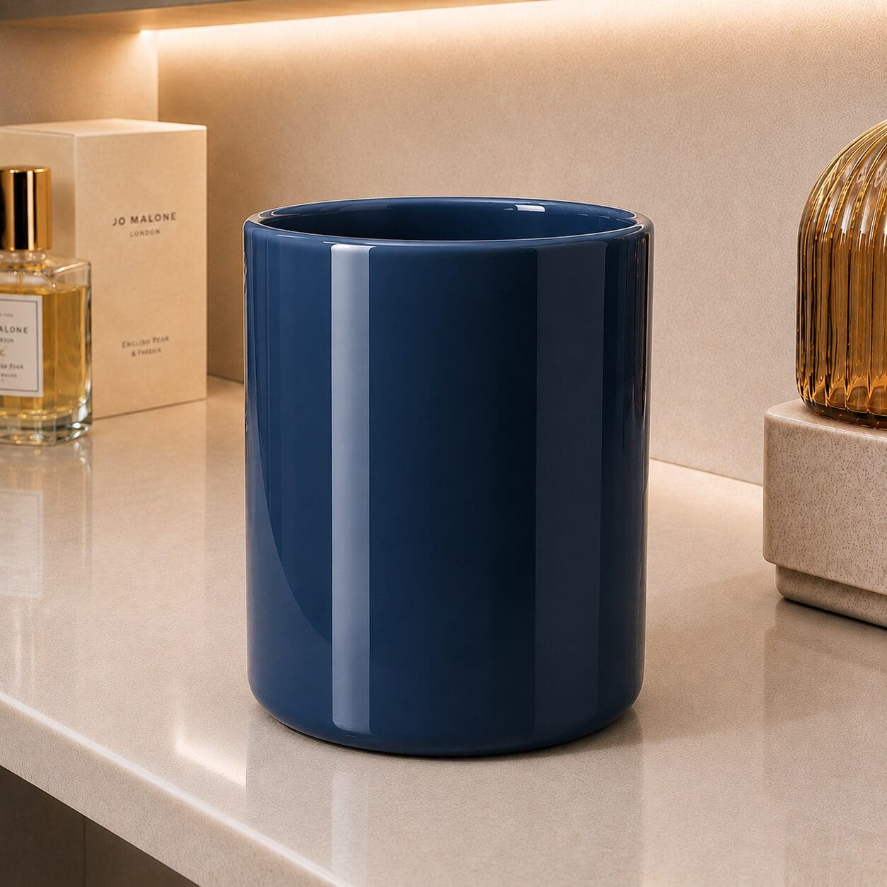 Navy blue cylindrical decorative container on beige surface with Jo Malone perfume bottle and gold ribbed vase nearby
