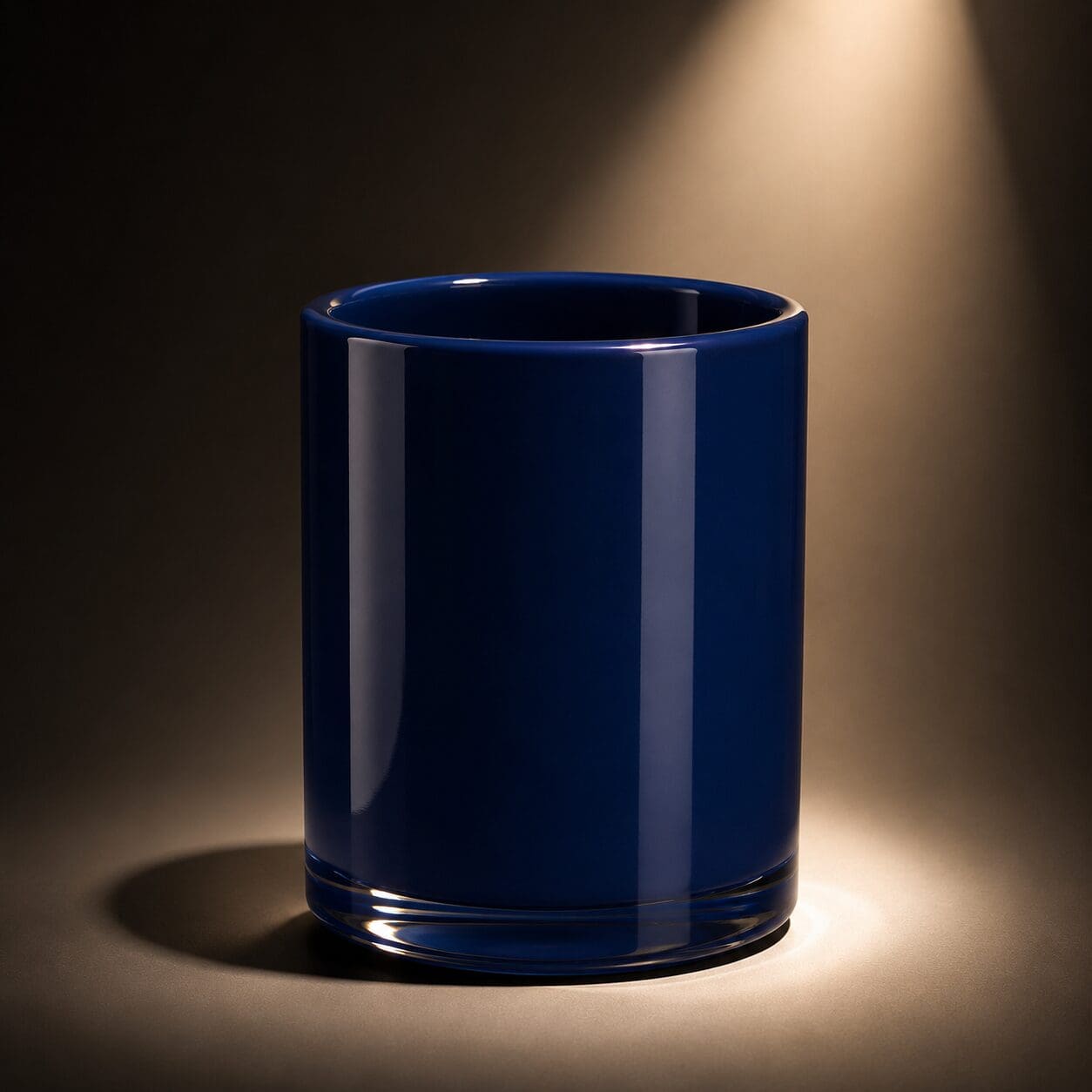 Empty navy blue cylindrical glass jar with polished rim, lit by warm spotlighting against neutral background