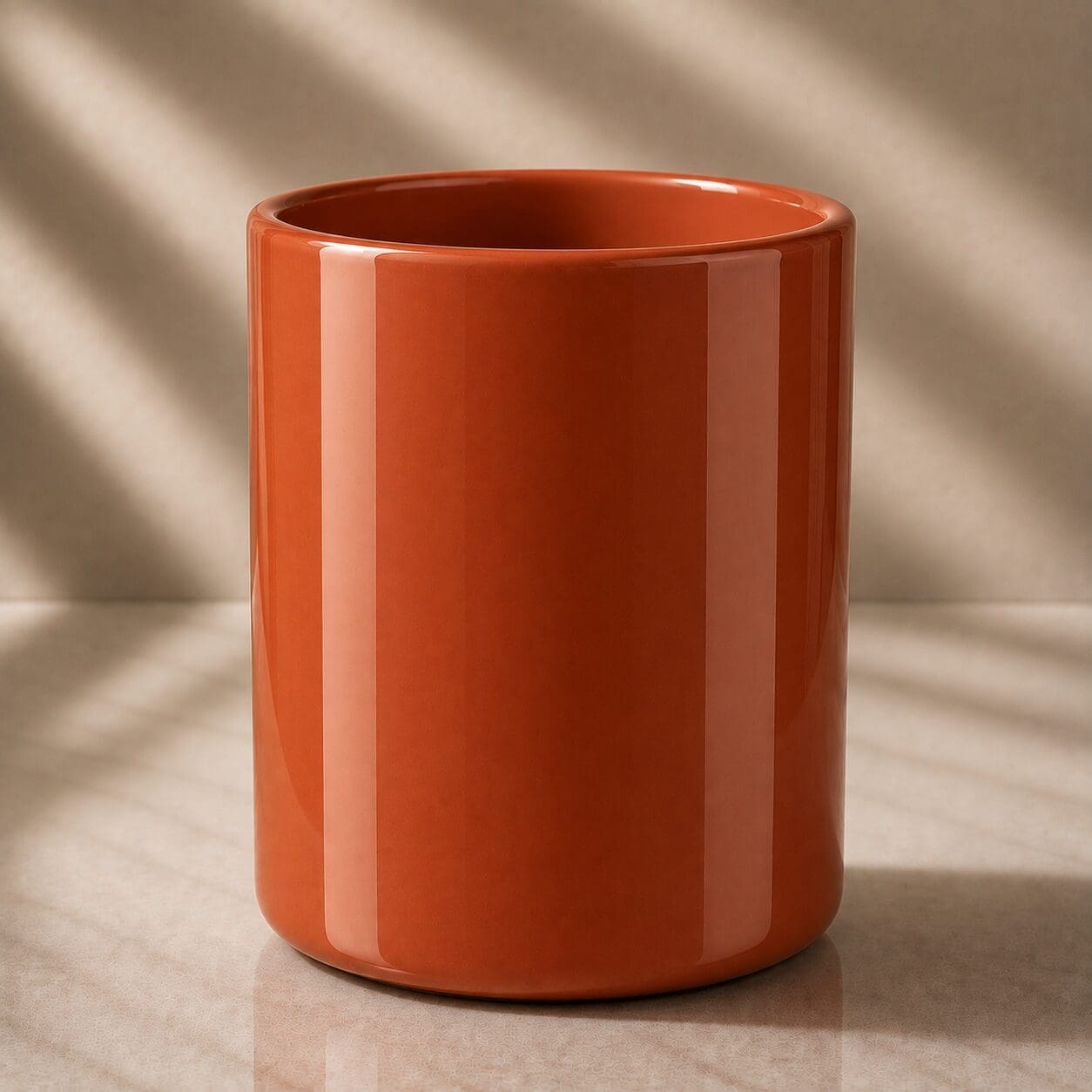 Glossy terracotta ceramic cylinder on a marble surface with natural light casting shadows in the background