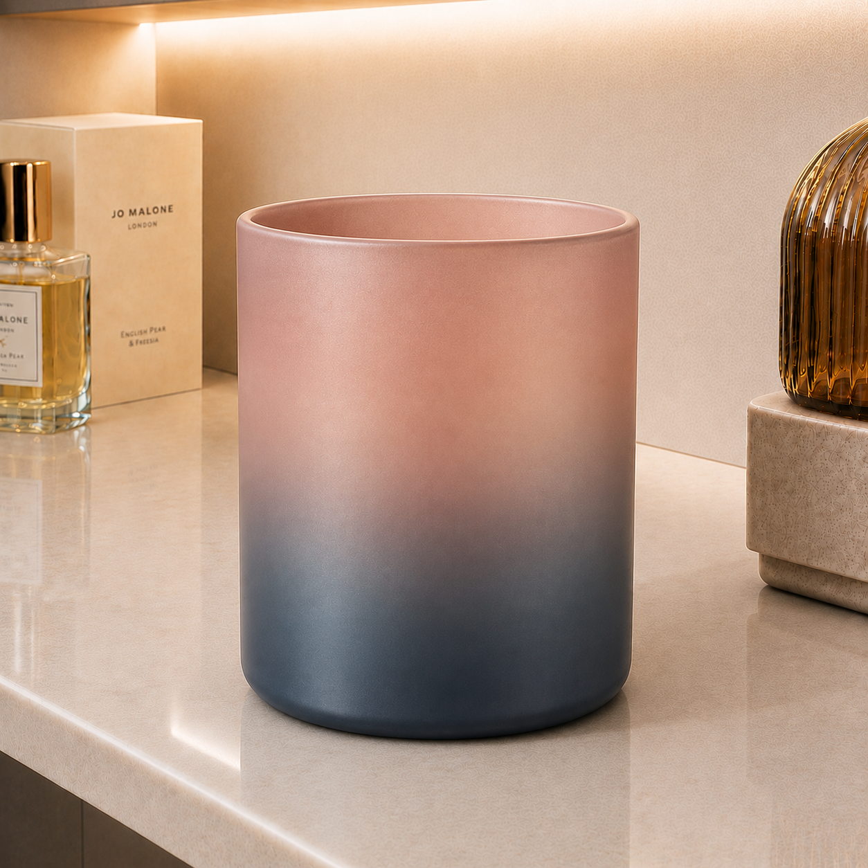 Gradient frosted glass candle jar transitioning from blush pink to charcoal gray, displayed on marble surface among luxury home decor items
