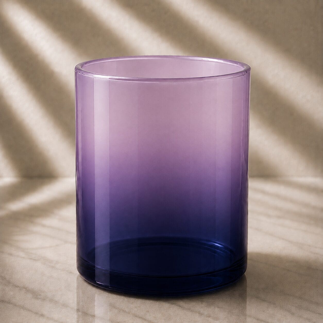 Purple ombre gradient glass cylinder vessel with dark navy base transitioning to pale lavender top, sitting on marble surface with soft natural light