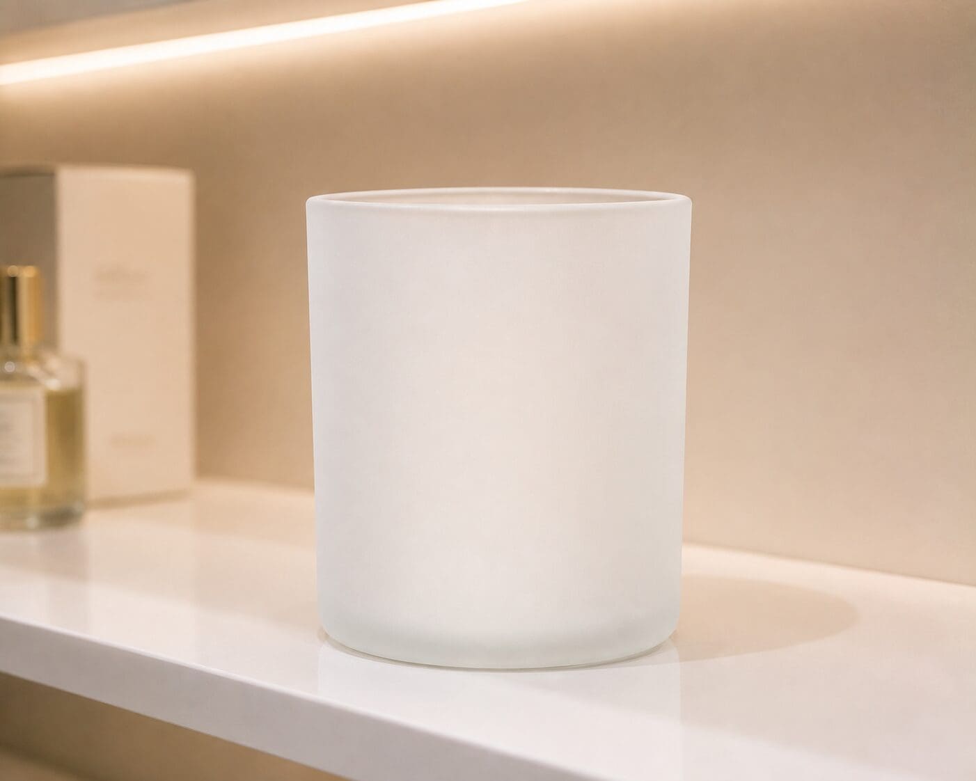 Frosted glass candle jar displayed on white shelf in minimalist bathroom setting with warm lighting