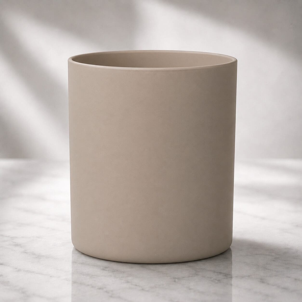 Blank beige ceramic cylinder on marble surface with soft natural lighting, suitable for candle jar decorating or glass screen printing services