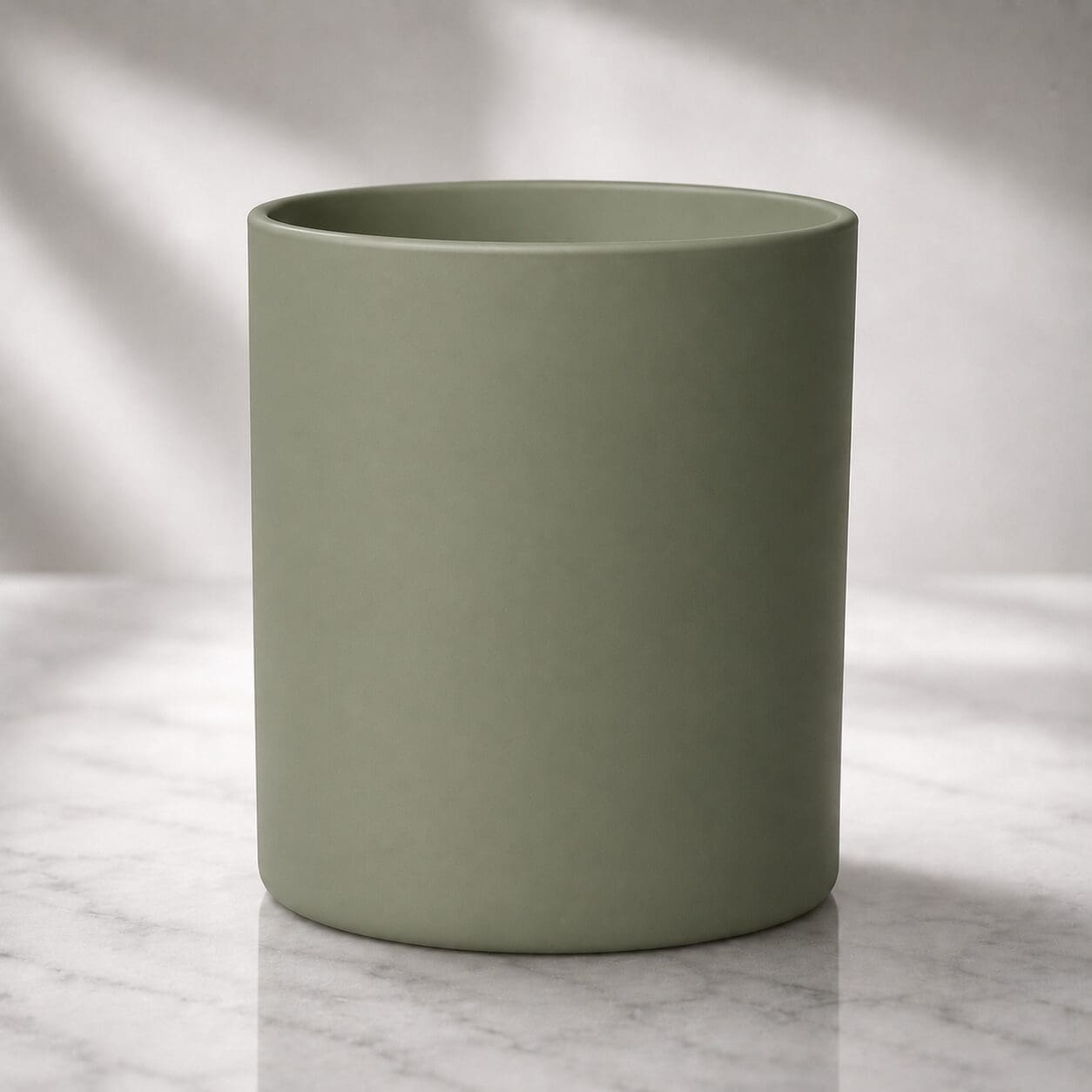 Sage green cylindrical ceramic vessel on marble surface with soft natural lighting, suitable for candle filling or decorative purposes