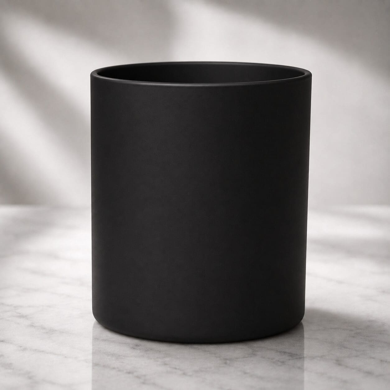 Black cylindrical matte ceramic mug on marble surface with soft natural lighting
