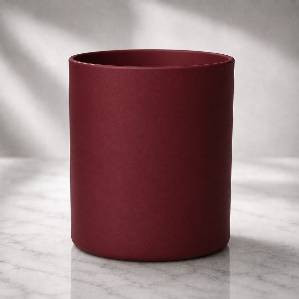 Deep burgundy cylindrical vessel on marble surface with soft natural lighting, suitable for candle filling or decorative glass customization