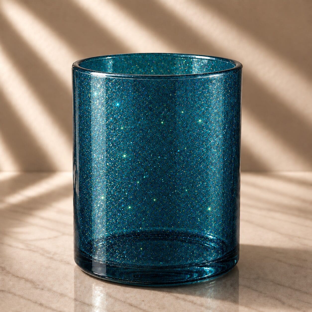 Teal glitter-coated cylindrical glass jar with spray coating and shimmering finish, displayed on light wood surface with natural shadows