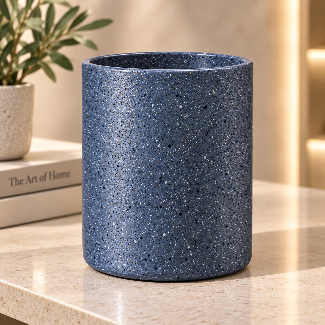 Blue speckled ceramic cylinder vase with metallic accents on wooden shelf, styled with potted plant and decorative books