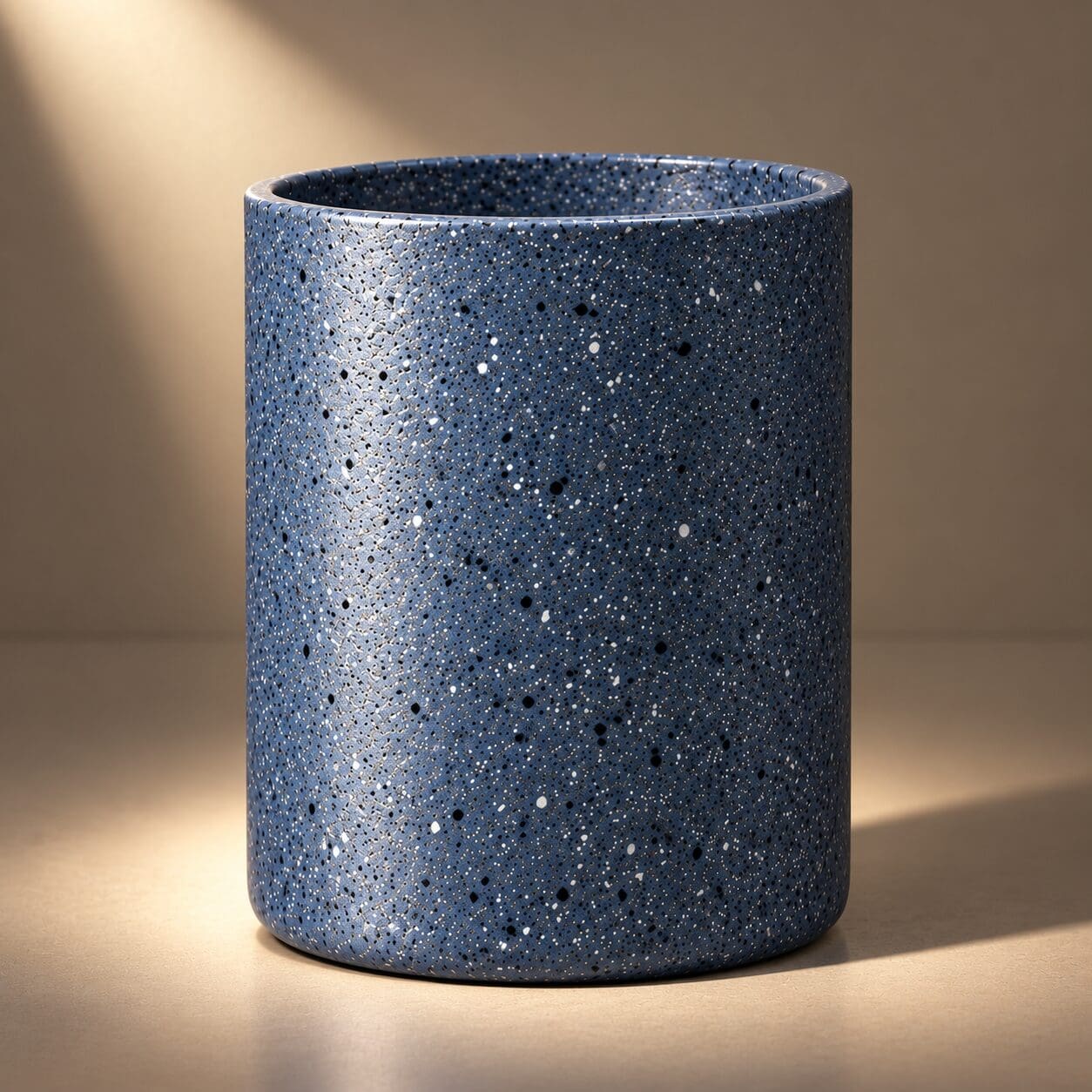 Blue speckled cylindrical candle jar with white and black speckle pattern, displayed with warm lighting on neutral background