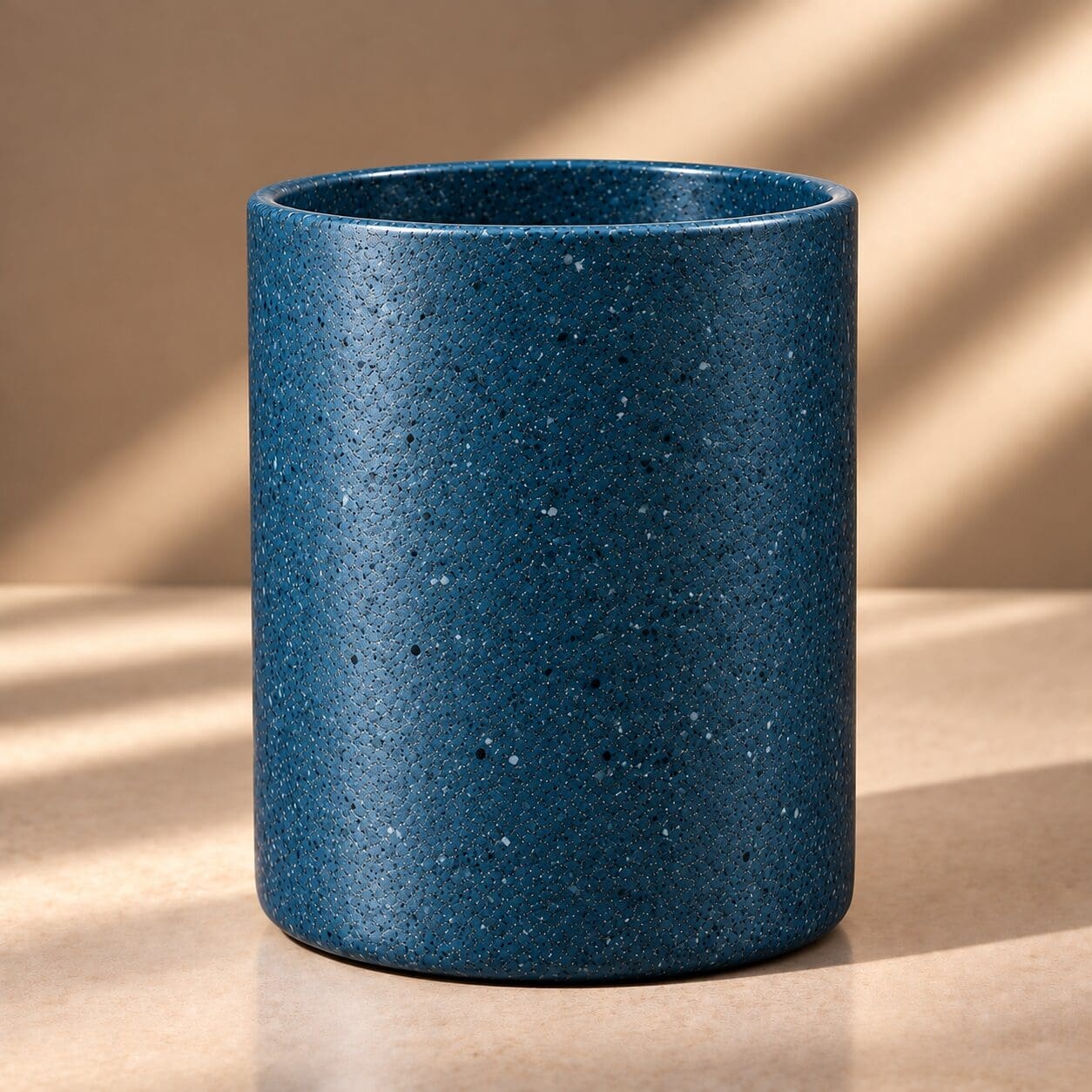 Blue speckled cylindrical candle jar with textured spray coating and white aggregate particles on neutral background with natural lighting