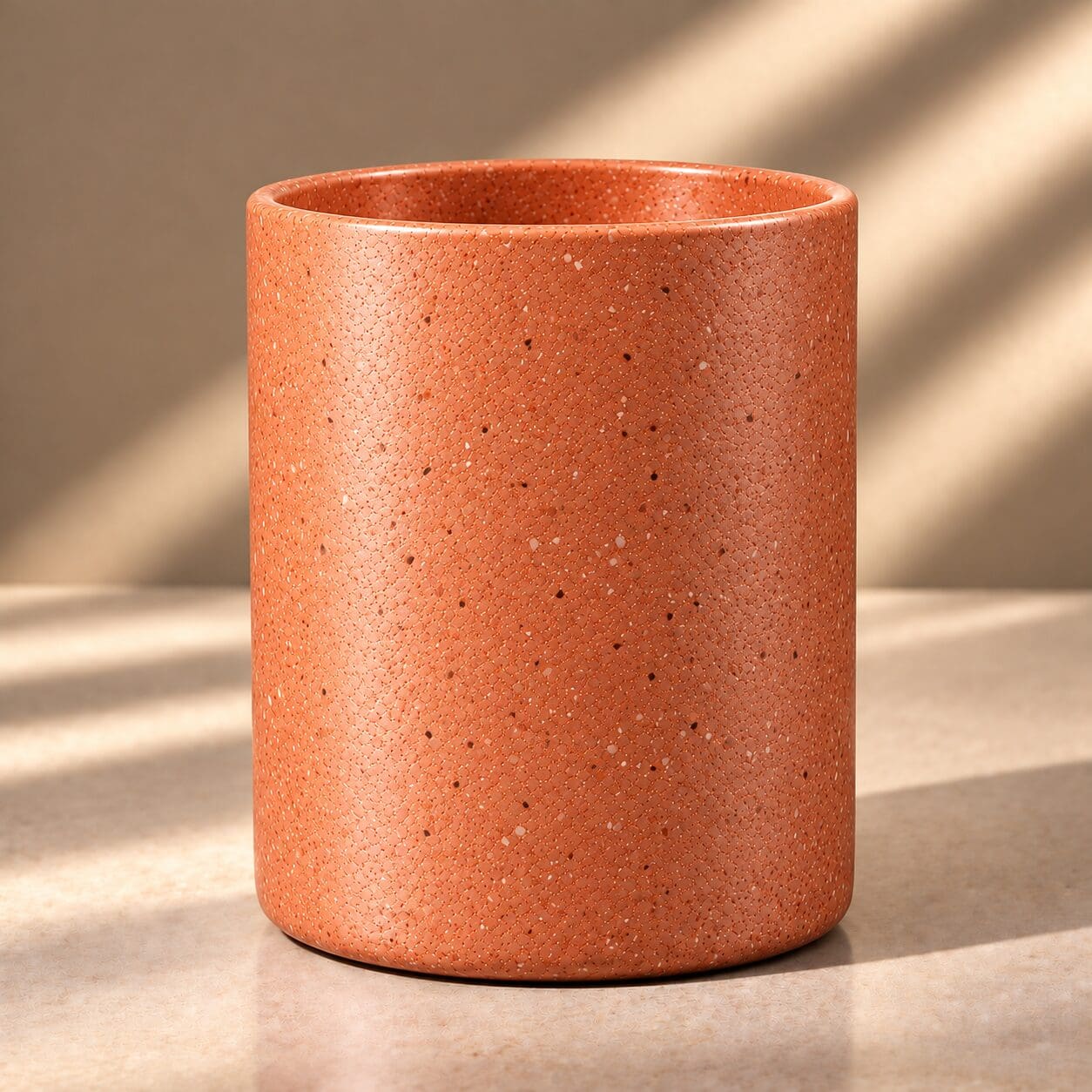 Terracotta speckled ceramic cylinder vessel with textured surface, casting shadows in natural light
