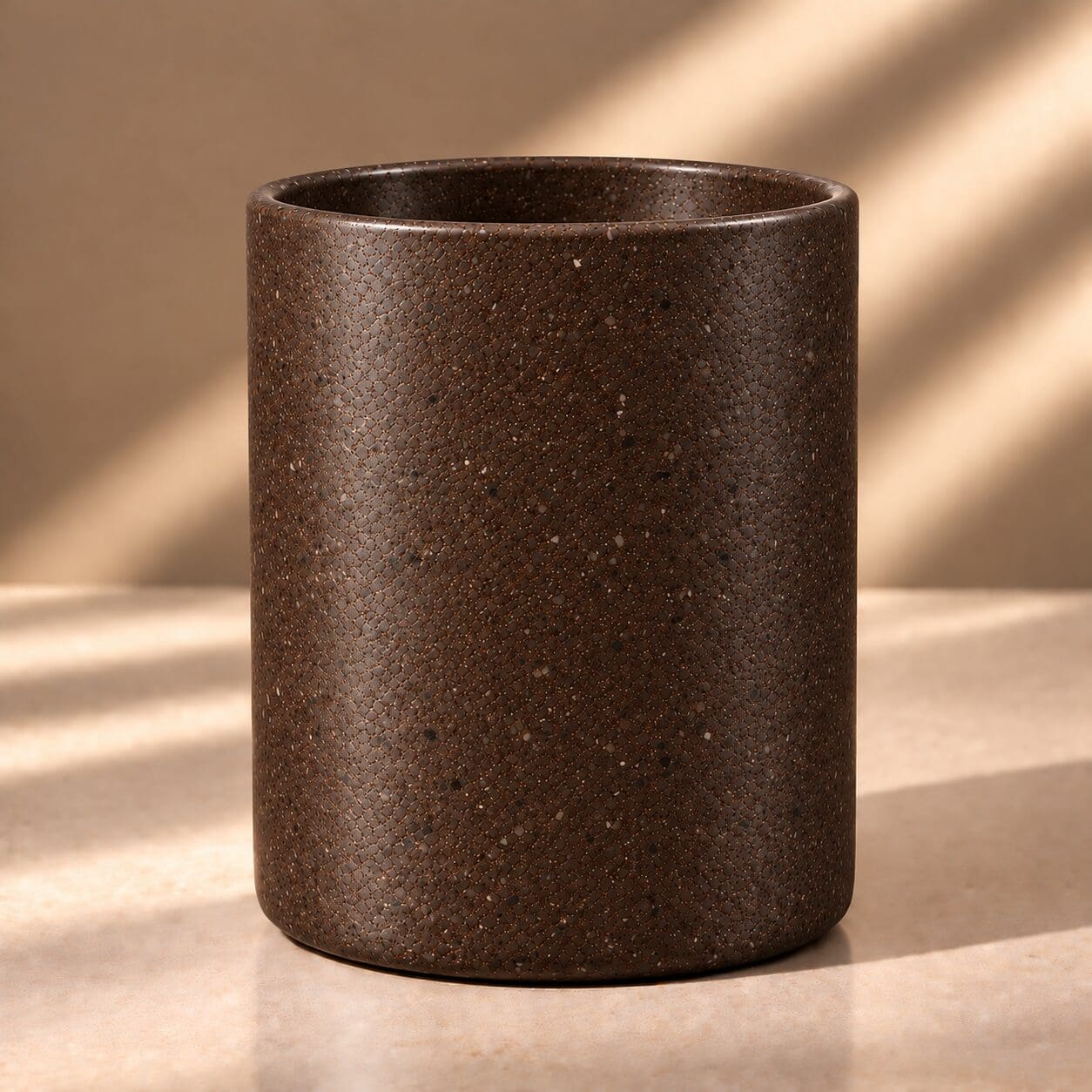 Dark brown speckled cylindrical ceramic vessel with textured surface casting shadows under natural light