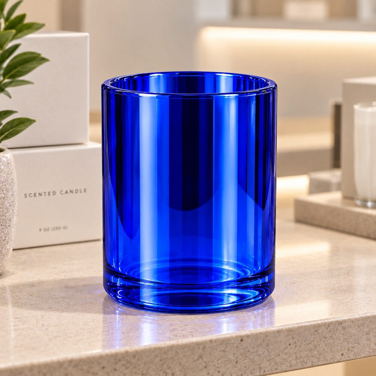 Bright blue cylindrical glass jar with vertical ribbed texture displayed on marble countertop, styled as decorative candle container or spray coated bottle with minimalist home decor setup