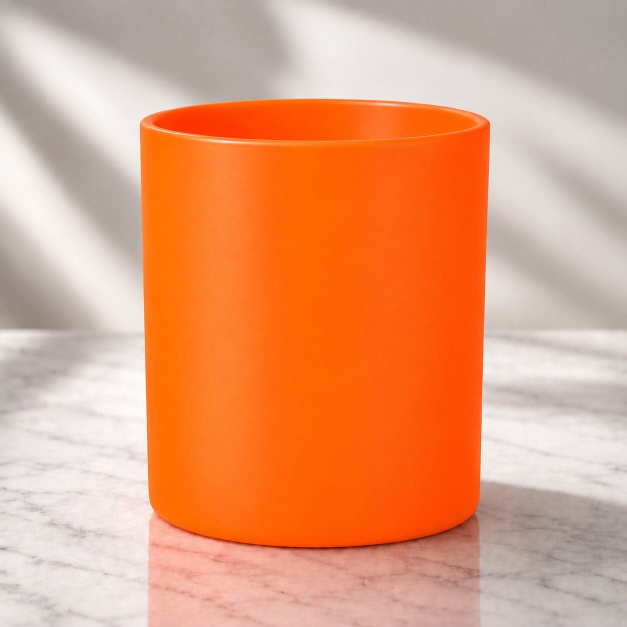 Bright orange ceramic mug with glossy spray coating displayed on marble surface with natural window light