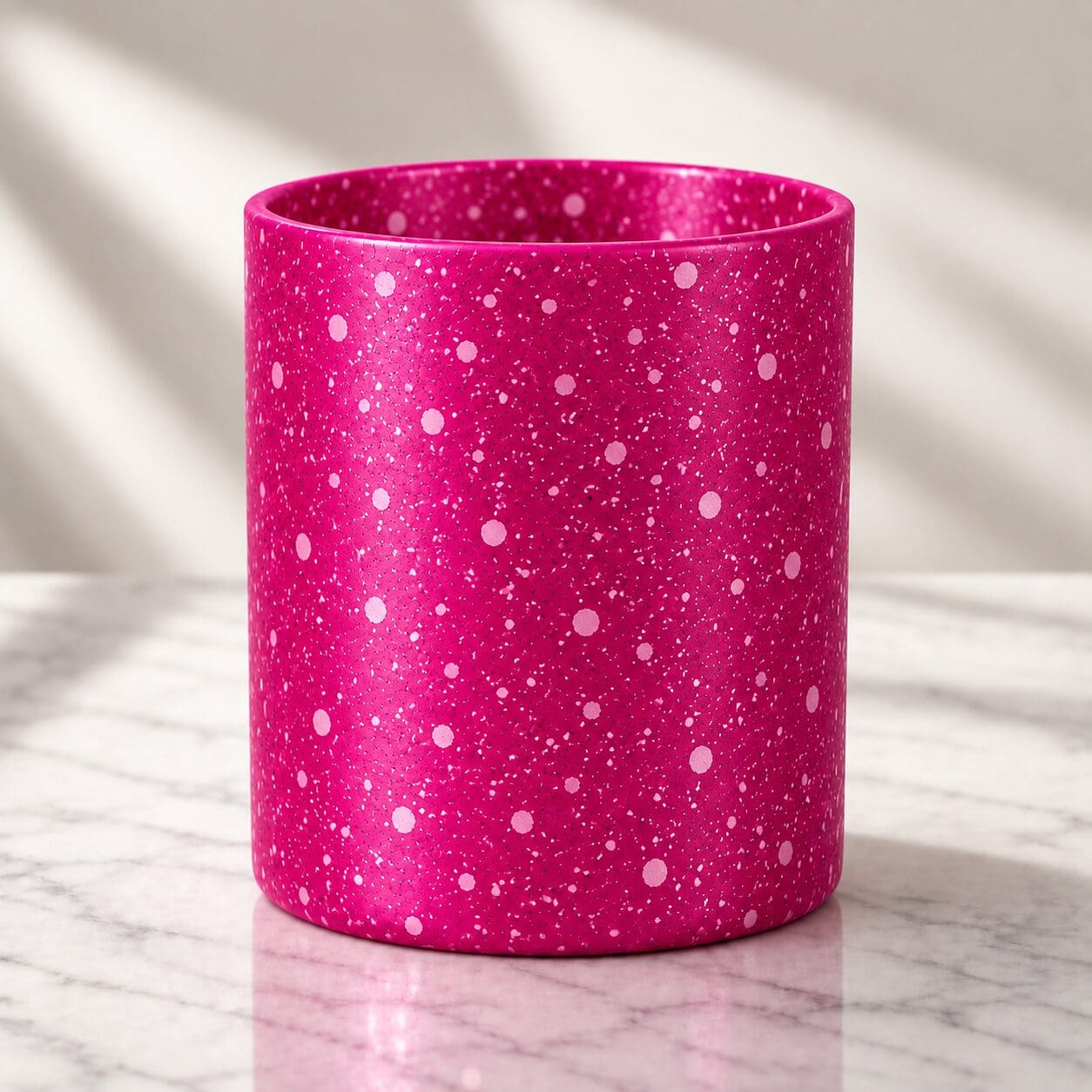 Bright pink glitter-coated cylindrical candle jar with white sparkle accents, sitting on marble surface with natural lighting