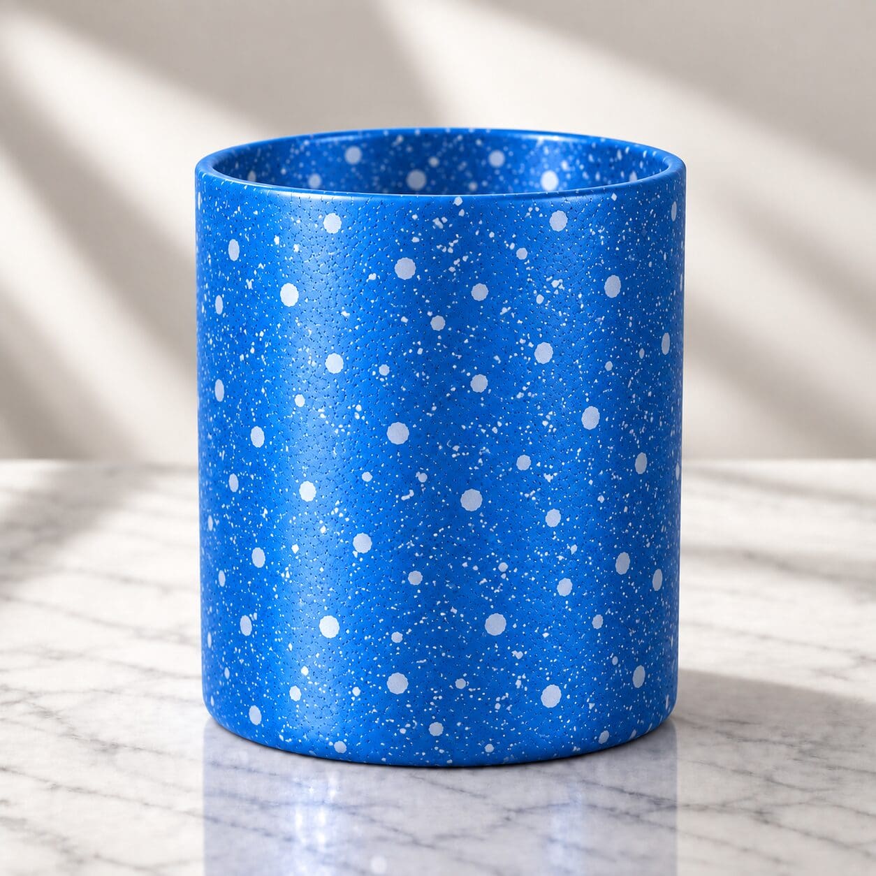 Blue speckled cylindrical container with white dots and spray coating on marble surface with natural lighting