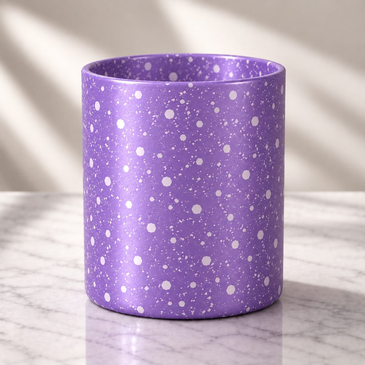 Purple cylindrical candle jar with white speckled spray coating and glitter effect on marble surface