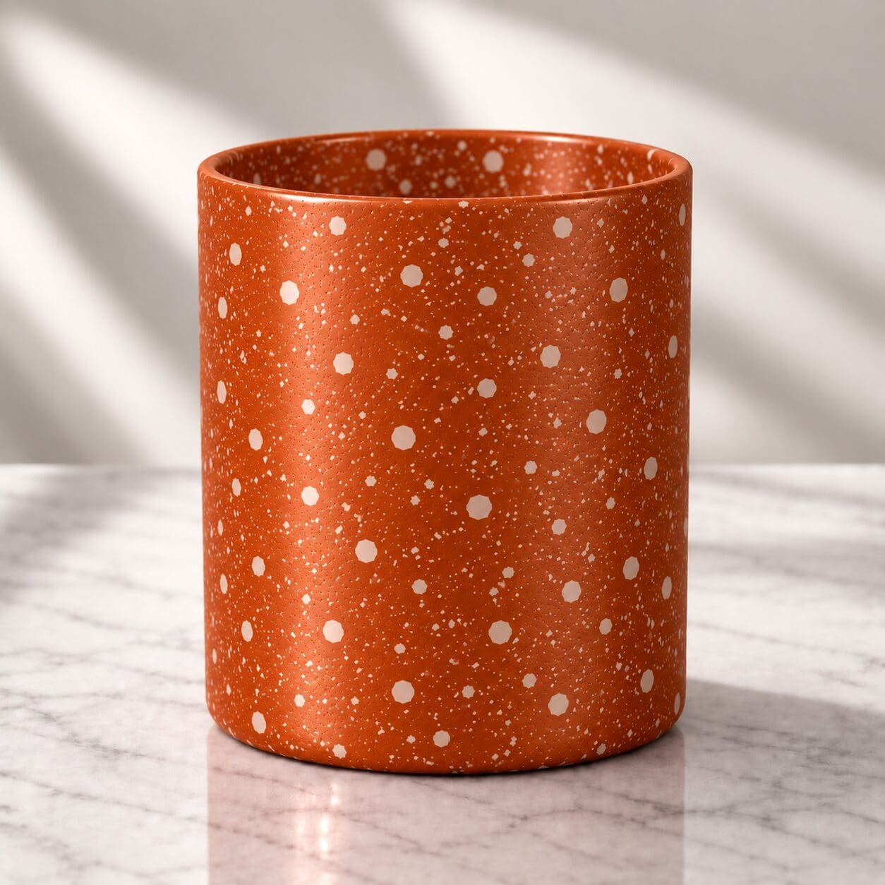 Rust-orange cylindrical container with white speckled spray coating pattern on marble surface with soft shadows