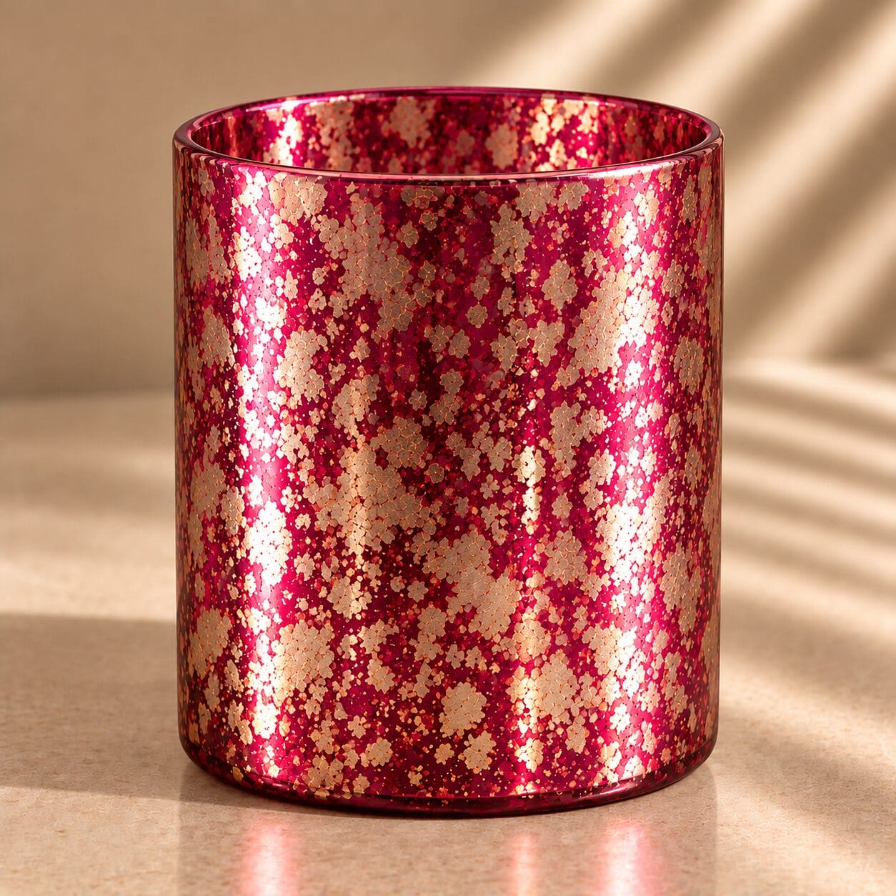 Red and gold glitter-coated cylindrical glass jar with spray coating finish, casting shadows on neutral background