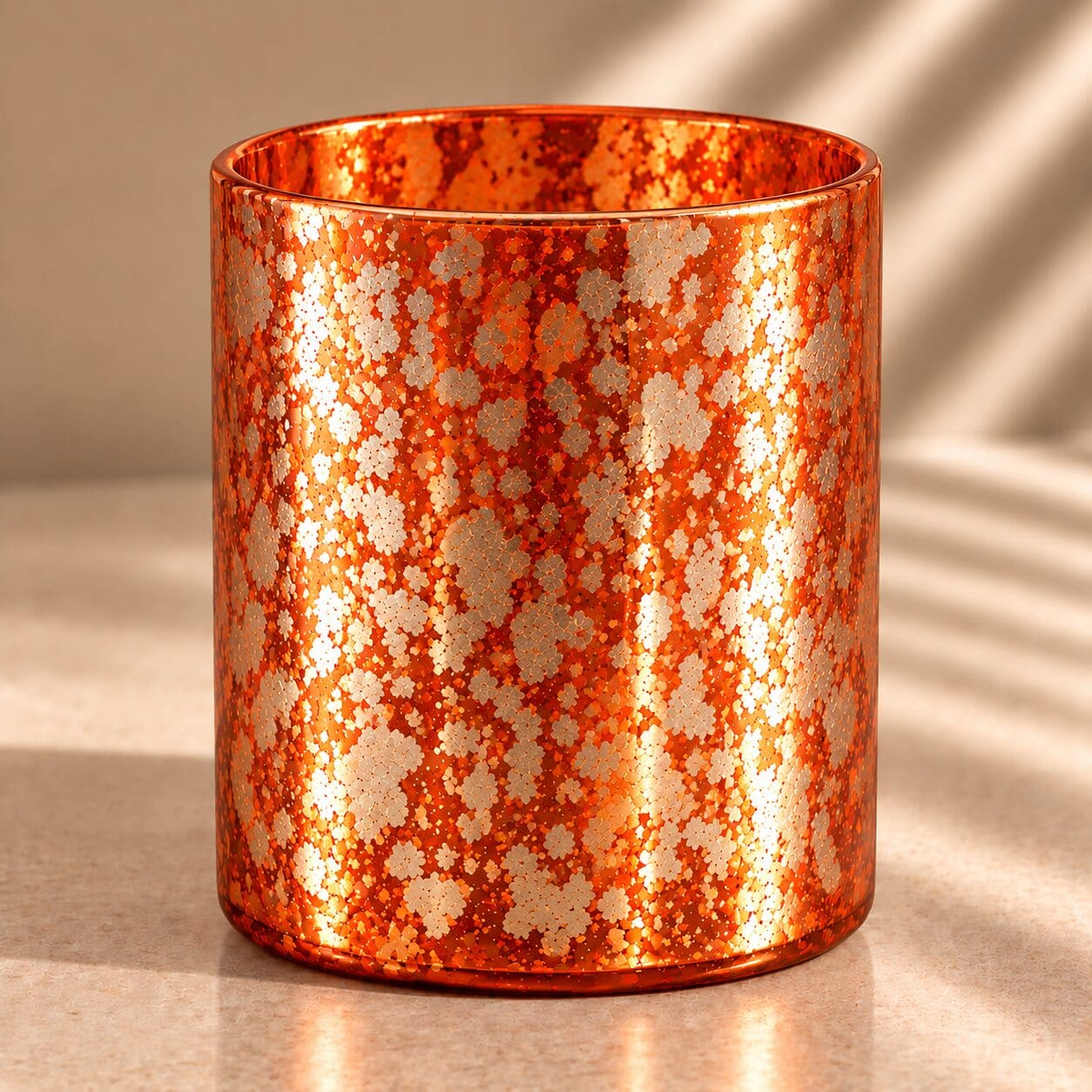 Orange glitter spray coated cylindrical glass jar with metallic finish, casting shadows on neutral background