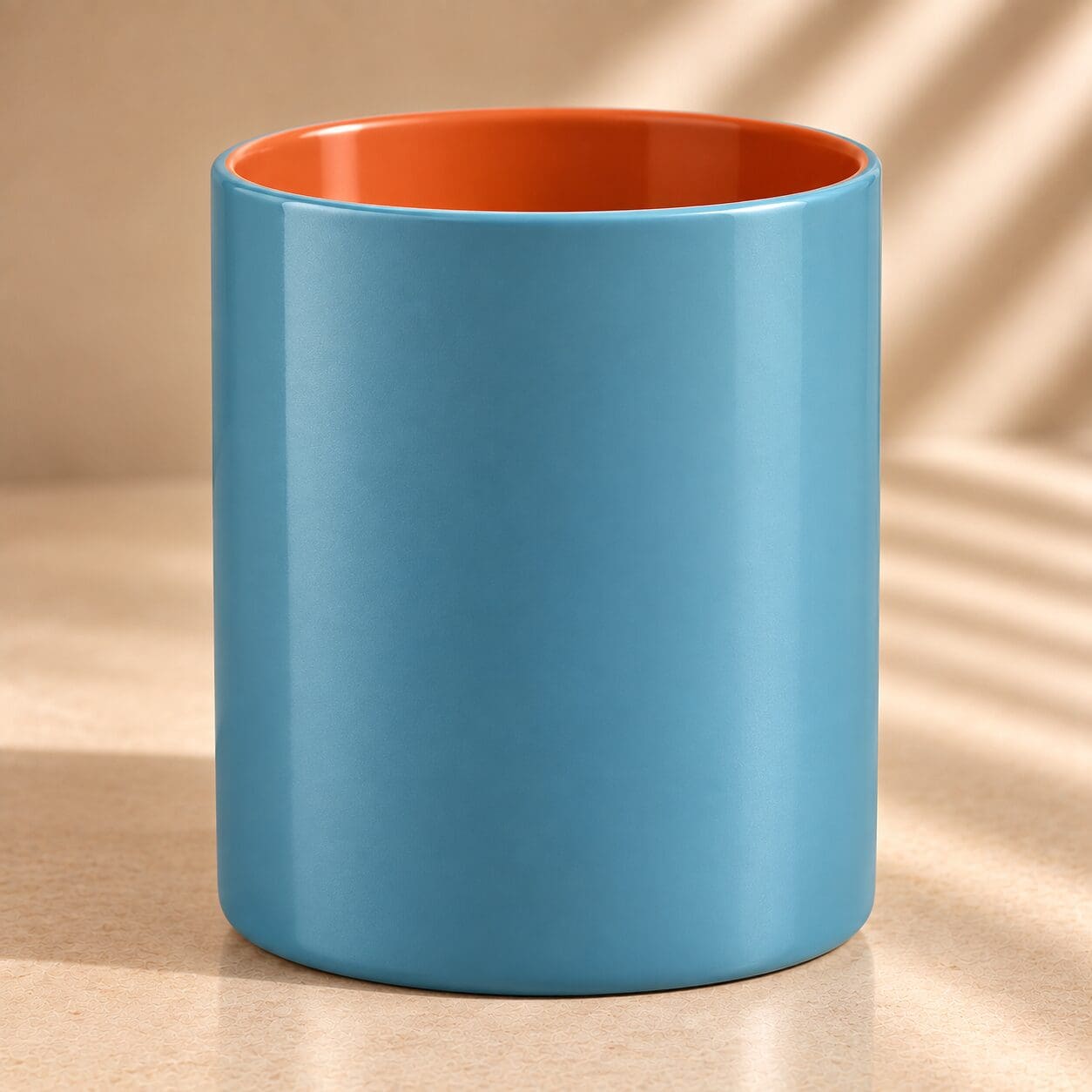 Turquoise ceramic mug with orange interior, displayed on beige surface with natural lighting