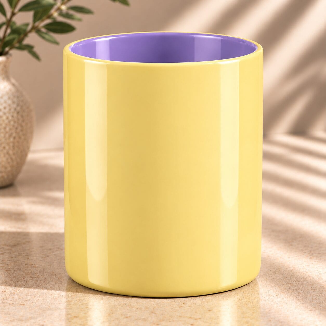 Yellow spray coated ceramic mug with purple interior, displayed on beige surface next to potted plant