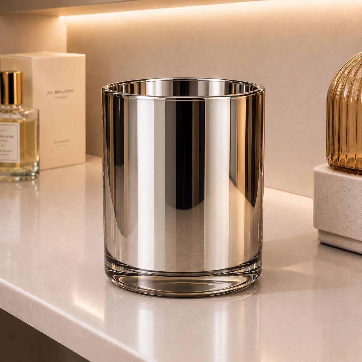 Luxury metallic striped glass candle jar displayed on a beige shelf with perfume bottles and decorative accessories in warm ambient lighting