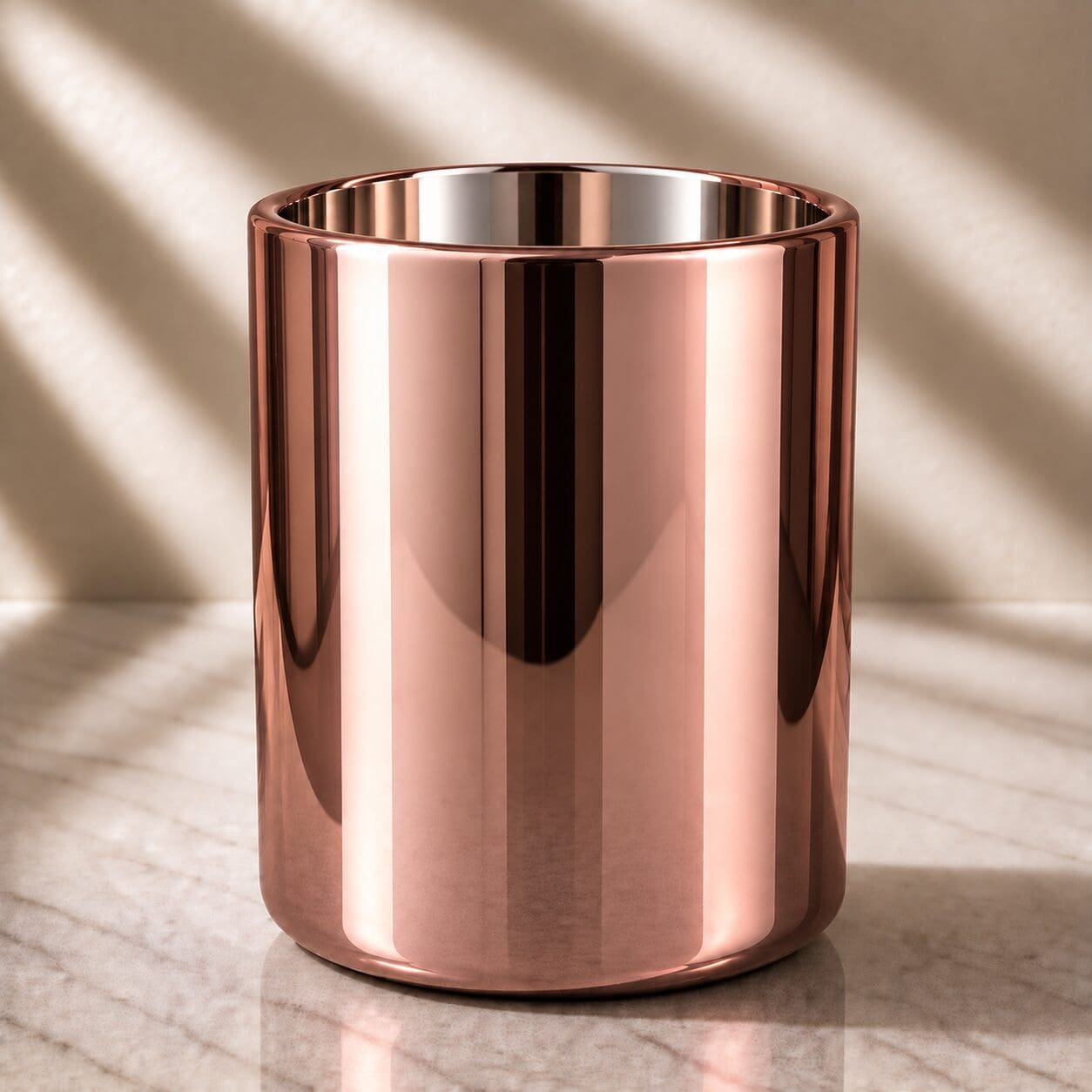 Polished rose gold cylindrical container with reflective metallic finish on marble surface with natural lighting